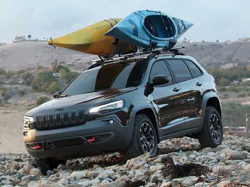 2023 Jeep Cherokee driving on a rocky path with two kayaks on roof rails